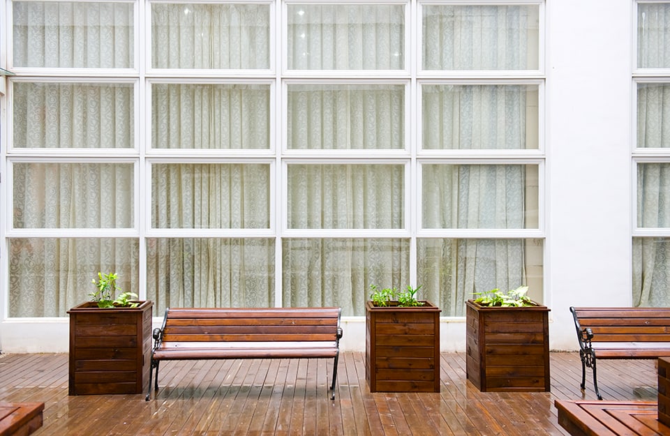 Decking esterno di un edificio bianco con pareti vetrate. All'esterno si vedono delle fioriere e una panchina in legno