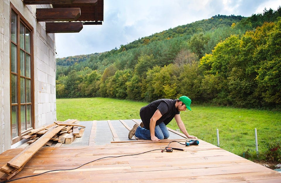 Un tecnico sta installando un parquet da esterno fuori da una casa immersa nel verde in una zona montuosa