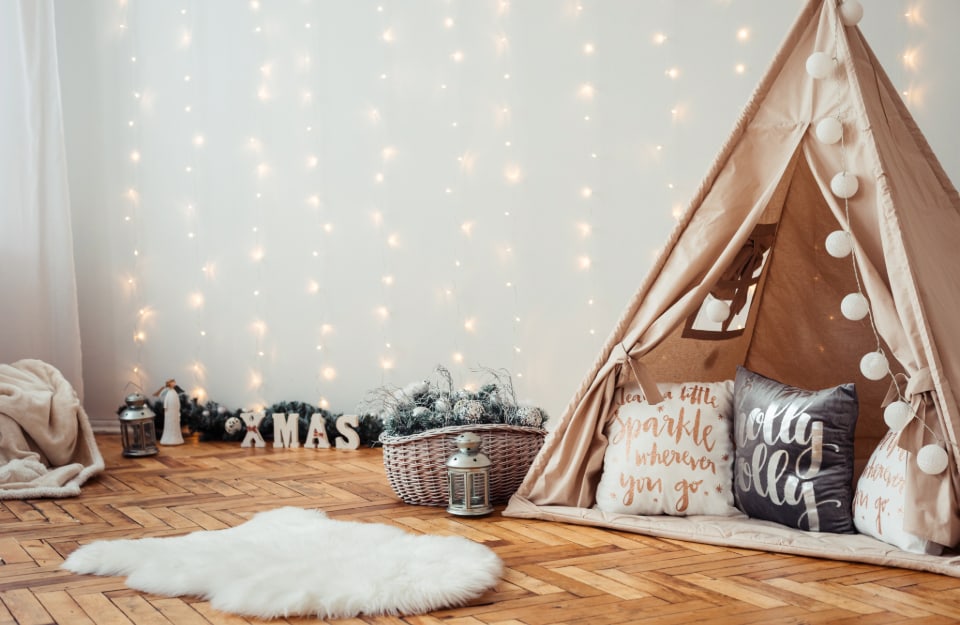 Cameretta dei bambini addobbata per Natale, con parquet, lucine che scendono dalla parete, tepee con tappeti e cuscini