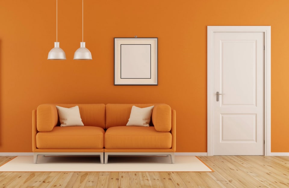 Una stanza con pareti e sofà arancione, porta bianca, parquet, tappeto e lampadari