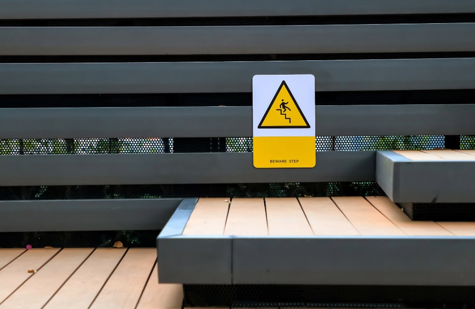 Un cartello che segnala di fare attenzione ai gradini in legno potenzialmente scivolosi su una scala esterna