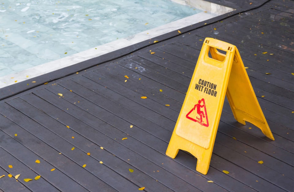 Un cartello giallo che indica il pericolo di pavimento scivoloso sul decking a bordo piscina