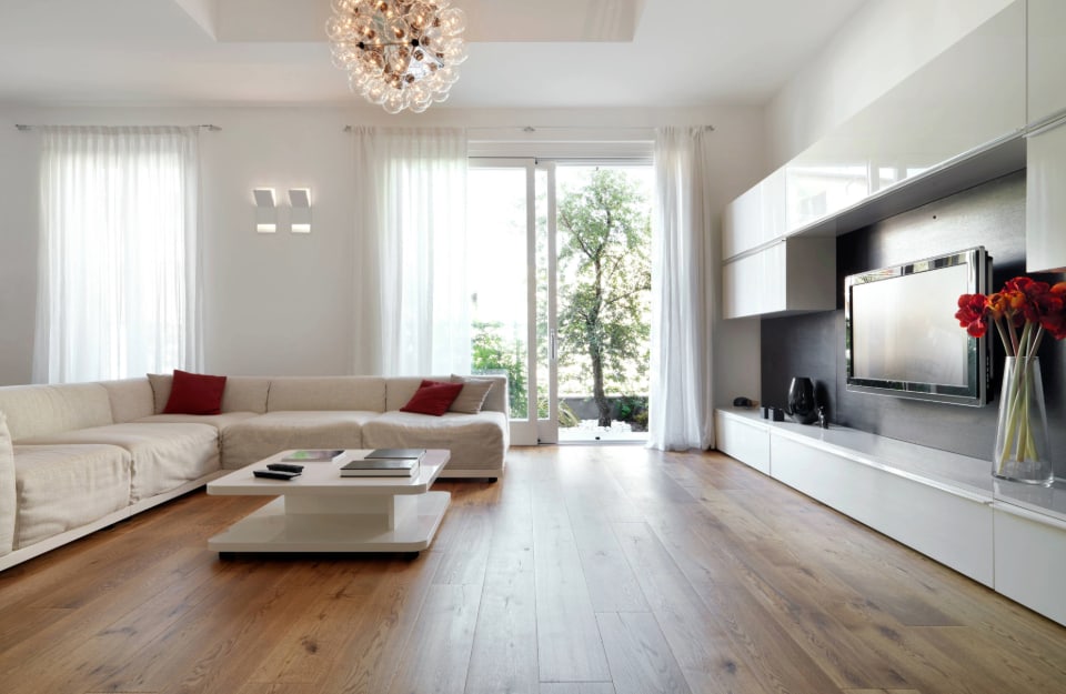 Salotto moderno in stile minimal tutto sui toni del bianco, con sofà, grande televisore, tavolino da caffè, due porte-finestra, lampadario di design e parquet a grandi plance