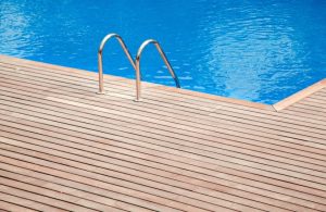 Una piscina con acqua blu e limpida. Sul bordo della piscina c'è un decking in teak. Al centro della piattaforma, c'è una scala in metallo con due corrimano curvi che scendono nell'acqua