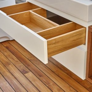 Un cassetto aperto con più scomparti all'interno. Il cassetto fa parte di un mobile della toeletta di un bagno con pavimento in teak