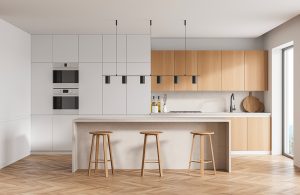 Cucina in stile essenziale moderno sui toni del bianco e del legno naturale, con parquet in rovere a spina di pesce, e bancone con tre sgabelli