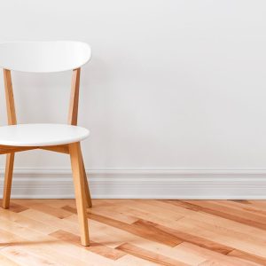 Sedia in stile modernista bianca e legno naturale, di fronte a un muro bianco e un parquet