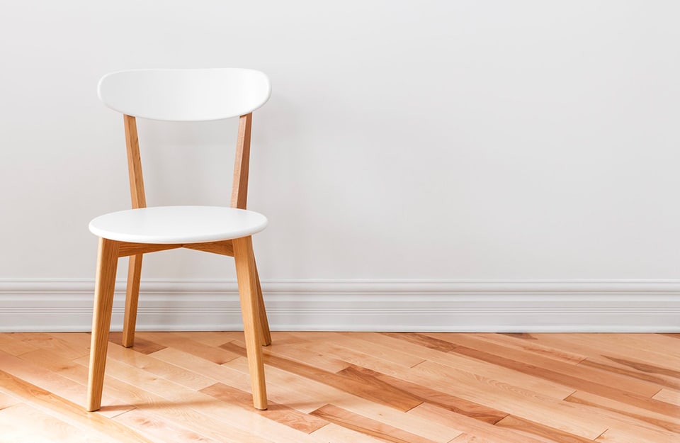 Sedia in stile modernista bianca e legno naturale, di fronte a un muro bianco e su un parquet posato diagonalmente