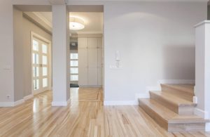 Ingresso di un'abitazione vuota con pavimento in parquet, pareti bianche, colonna e scale