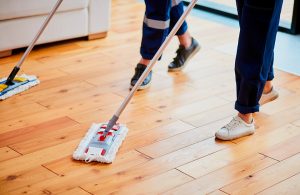 Due persone, delle quali si vedono solo gambe e piedi, puliscono un parquet in legno