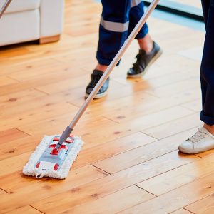 Due persone, delle quali si vedono solo gambe e piedi, puliscono un parquet in legno