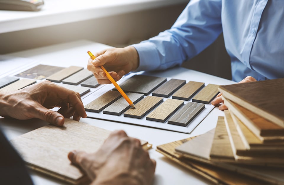 Dettaglio di un momento dell'acquisto di un parquet. Si vedono le mani di un venditore che mostra i campioni, e quelle di un cliente che sta ad ascoltare