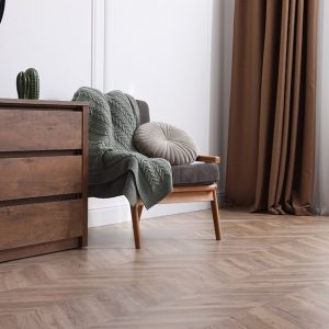 Area di un salotto elegante e minimal con parquet in legno a spina di pesce. Si vedono una cassettiera, una poltrona e uno specchio