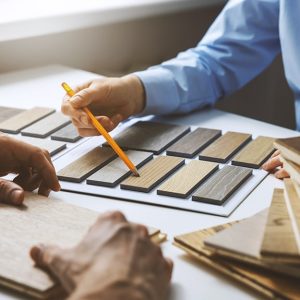 Dettaglio di un momento dell'acquisto di un parquet. Si vedono le mani di un venditore che mostra i campioni, e quelle di un cliente che sta ad ascoltare