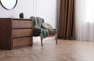 Area di un salotto elegante e minimal con parquet in legno a spina di pesce. Si vedono una cassettiera, una poltrona e uno specchio