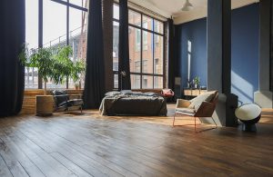Grande open space con letto e poltrona. La luce entra da due grandi finestre che arrivano fino a terra. Il pavimento è un parquet rustico