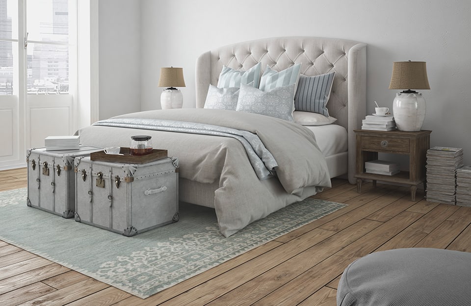 Camera da letto con parquet rustico. Sotto al letto c'è un grande tappeto, in fondo un due bauli, usati anche come tavolini da caffè. Accanto ai comodini ci sono pile di libri