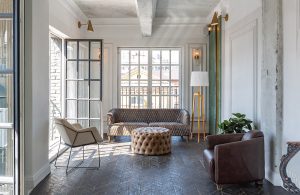 Salotto moderno che presenta una commistione di stili, abbinando sofa e poltrone vintage e moderniste, una grande lampada in stile scandinavo, pareti bianche decorate e altre lasciate grezze