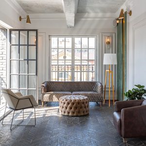 Salotto moderno che presenta una commistione di stili, abbinando sofa e poltrone vintage e moderniste, una grande lampada in stile scandinavo, pareti bianche decorate e altre lasciate grezze