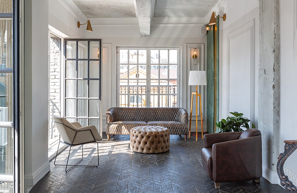 Salotto moderno che presenta una commistione di stili, abbinando sofa e poltrone vintage e moderniste, una grande lampada in stile scandinavo, pareti bianche decorate e altre lasciate grezze