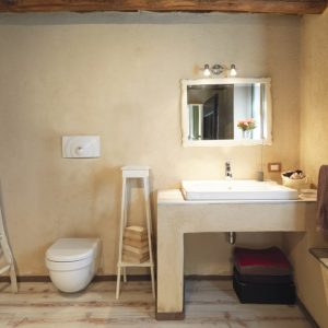 Bagno con elementi naturali: pietra, legno, metallo, travi a vista. Una vecchia scala dipinta di bianco appoggiata alla parete funge da porta asciugamani
