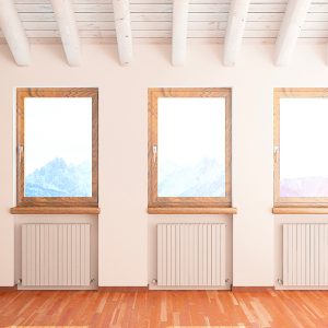 Mansarda di montagna con pavimento in parquet. Si vedono tre finestre affacciate sul panorama, con sotto tre termosifoni. Il soffitto è con travi a vista bianche e c'è una parete in pietra