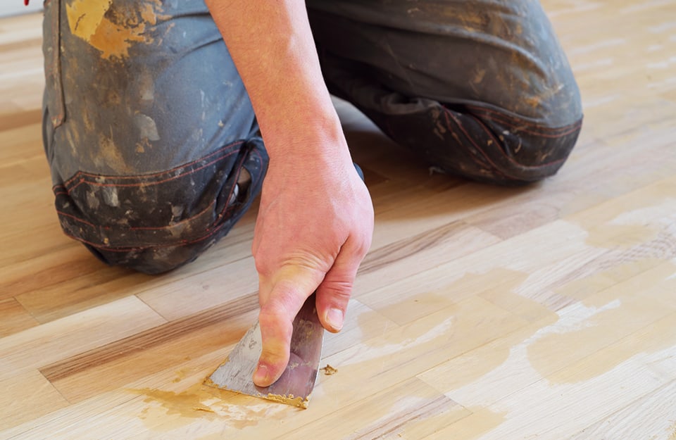 Un professionista ripara il parquet con lo stucco usando una spatola
