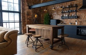 Cucina open space in stile industriale, con parquet rustico, bancone in legno, sgabelli in metallo e legno, grandi finestre, pareti con mattoncini a vista
