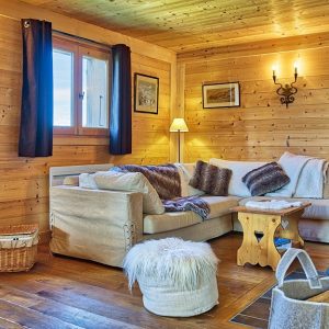 Salotto rustico da baita. Pavimento e pareti sono interamente in legno, le luci sono calde, ci sono una grande stufa blu in ghisa, un sofà d'angolo e un tavolino da caffè pure in stile rustico