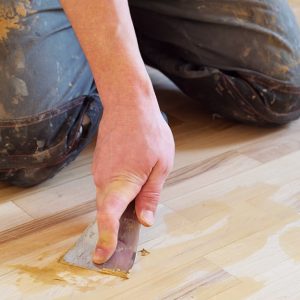 Un professionista ripara il parquet con lo stucco usando una spatola