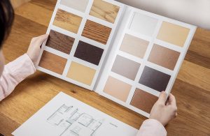 Una donna consulta un catalogo con le diverse essenze del parquet. Si vede anche la planimetria di un appartamento