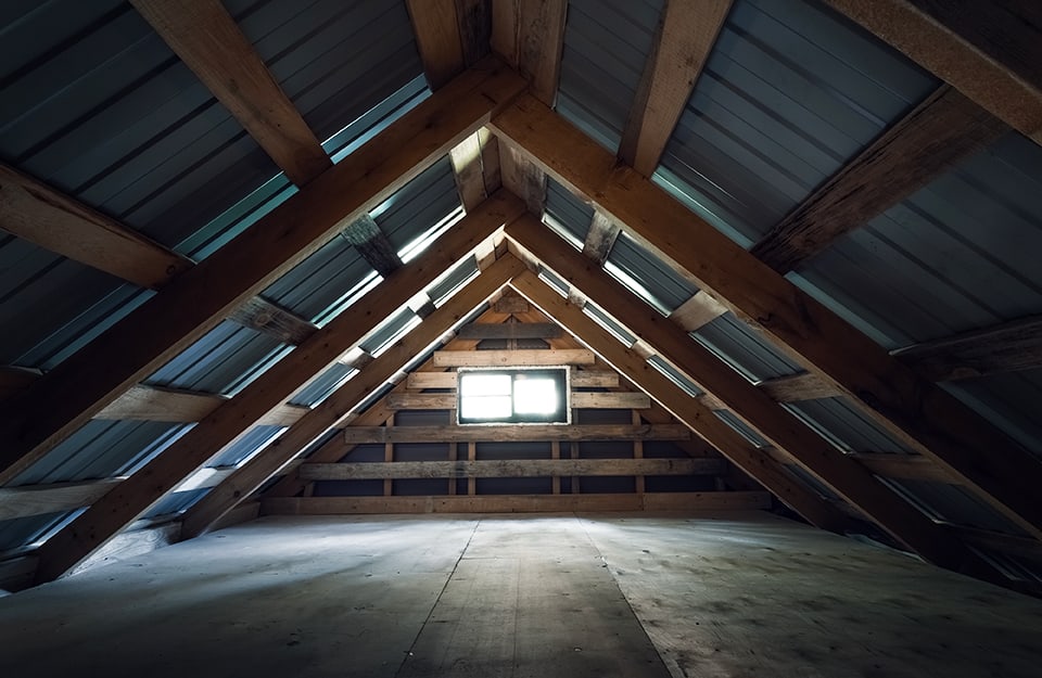 Vista in prospettiva centrale di una soffitta: si vedono le assi del tetto, una finestra in fondo e le assi di legno del pavimento