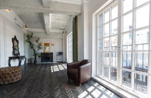 Un luminoso appartamento con pareti bianche, soffitto con travi a vista, grandi finestroni e parquet scuro a spina di pesce