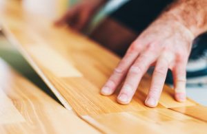 Prima piano della mano di un uomo che posa un parquet a incastro sopra alle piastrelle