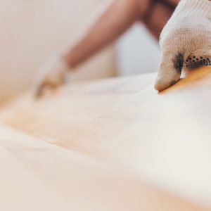 Prima piano della mano di un uomo che posa un parquet a incastro sopra alle piastrelle