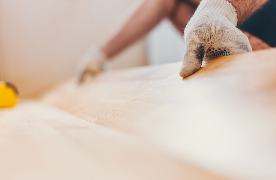 Prima piano della mano di un uomo che posa un parquet a incastro sopra alle piastrelle