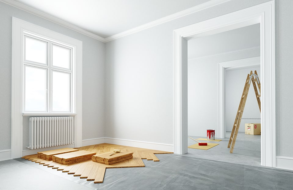 Stanza vuota e luminosa con un parquet parzialmente posato. Nell'altra stanza si intravede una scala