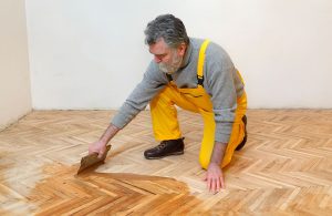 Un professionista applica con una spatola la vernice a un parquet