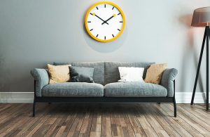Salotto moderno con sofà frigio, lampada su treppiede, parquet e un grande orologio giallo da parete