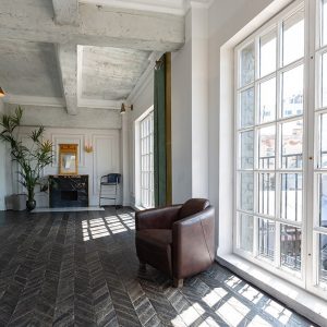 Un luminoso appartamento con pareti bianche, soffitto con travi a vista, grandi finestroni e parquet scuro a spina di pesce