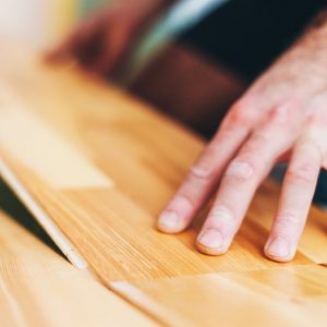 Prima piano della mano di un uomo che posa un parquet a incastro sopra alle piastrelle
