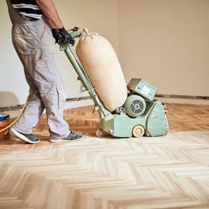 Un professionista si occupa della lamatura di un parquet usando una macchina levigatrice elettrica
