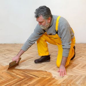 Un professionista applica con una spatola la vernice a un parquet