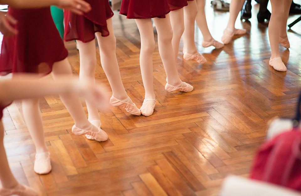 Primo piano su gambe e piedi di ragazzine in una scuola di ballo che si allenano su un pavimento in parquet