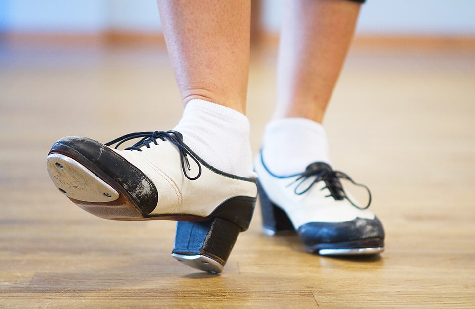Primo piano sulle caratteristiche scarpe di una ballerina di tip-tap che danza su un parquet