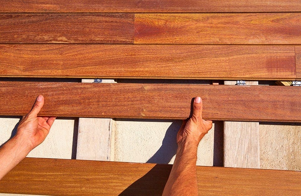 Le mani di un operaio sistemano le assi di legno ipe per il decking