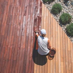 Visuale dall'alto di un giardino con ampio decking in legno di ipe, che una donna sta trattando con l'apposito olio impregnante