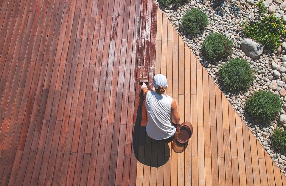 Visuale dall'alto di un giardino con ampio decking in legno di ipe, che una donna sta trattando con l'apposito olio impregnante