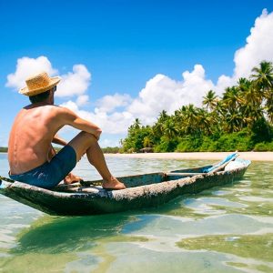 Uomo a torso nudo seduto rilassato su una piroga artigianale davanti a un'isola tropicale