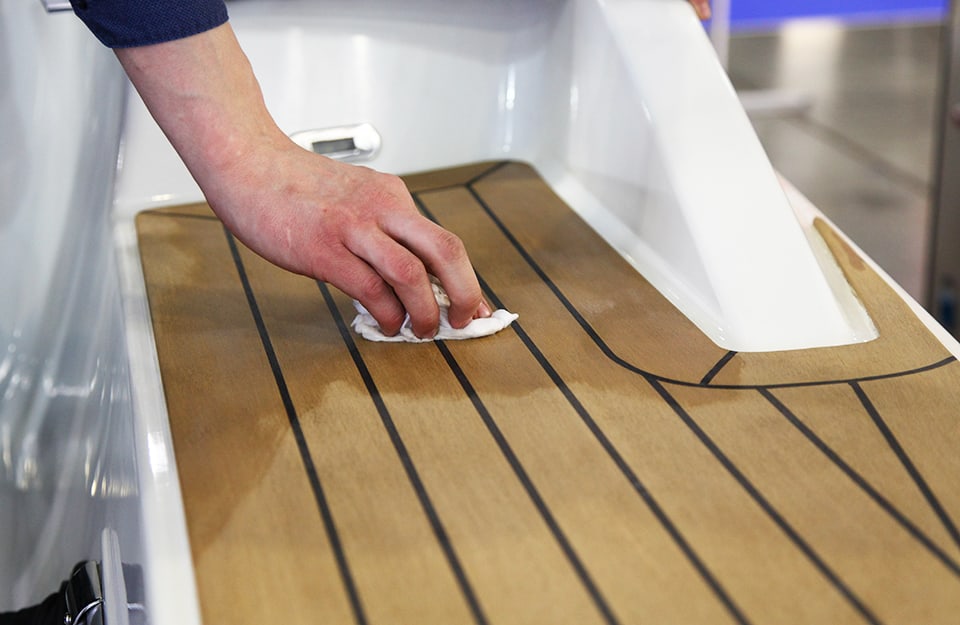 La mano di un uomo pulisce il ponte in legno di uno yacht usando un detergente